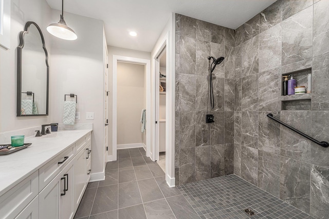 full bathroom featuring a spacious closet, a tile shower, vanity, and baseboards