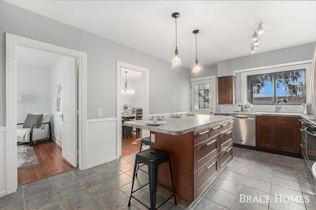 kitchen with pendant lighting, stainless steel dishwasher, wainscoting, a kitchen island, and a kitchen bar