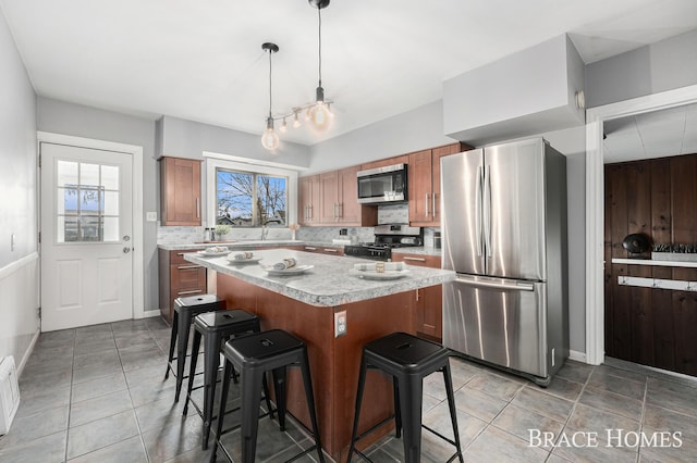 kitchen with light countertops, backsplash, appliances with stainless steel finishes, brown cabinetry, and a kitchen island