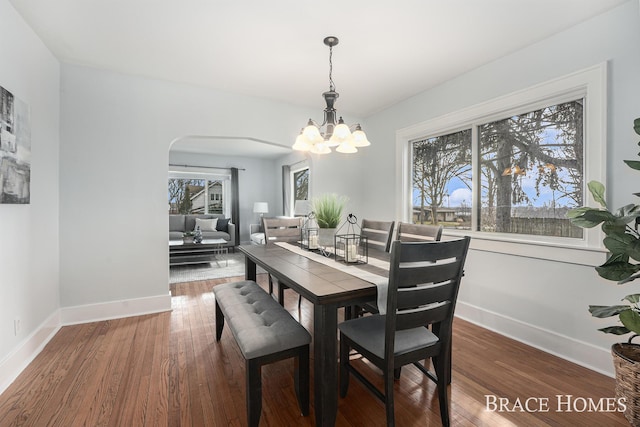 dining space featuring arched walkways, plenty of natural light, baseboards, and wood finished floors