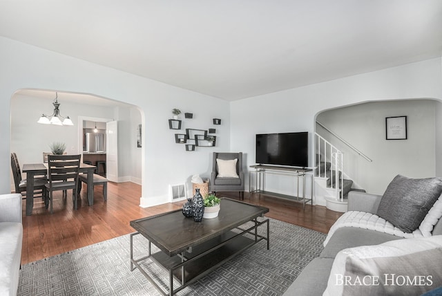 living room with arched walkways, visible vents, stairway, an inviting chandelier, and wood finished floors