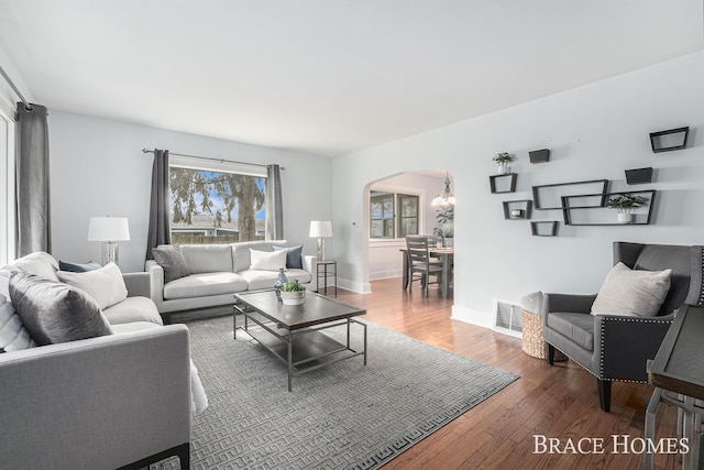 living area featuring arched walkways, visible vents, baseboards, wood-type flooring, and an inviting chandelier