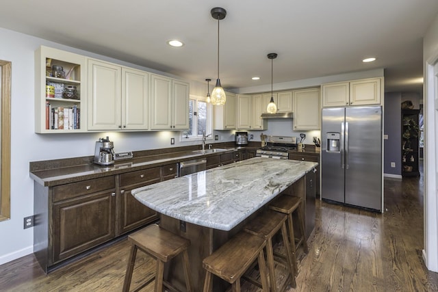 kitchen featuring dark wood-style floors, stainless steel appliances, cream cabinets, a sink, and a kitchen breakfast bar