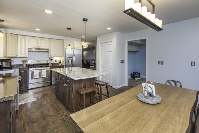 kitchen with dark wood-style floors, cream cabinets, stainless steel appliances, dark brown cabinets, and under cabinet range hood