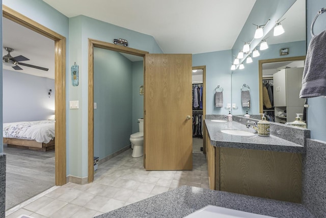 bathroom with ceiling fan, toilet, a sink, double vanity, and a walk in closet