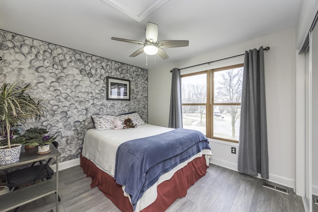 bedroom with baseboards, an accent wall, wood finished floors, and wallpapered walls