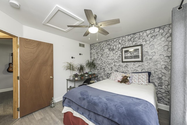 bedroom featuring visible vents, baseboards, light wood-type flooring, attic access, and wallpapered walls