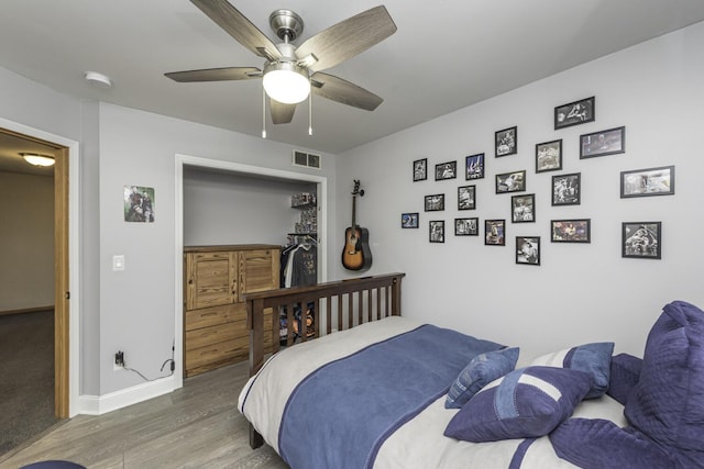 bedroom with a ceiling fan, visible vents, baseboards, and wood finished floors