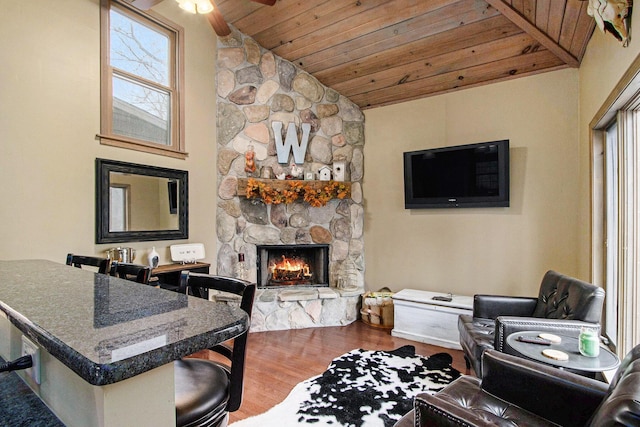 living room with ceiling fan, wood ceiling, lofted ceiling, a stone fireplace, and wood finished floors