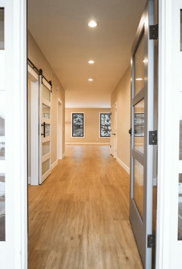 corridor with baseboards, a barn door, light wood-style flooring, and recessed lighting