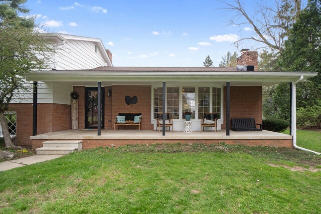 rear view of property with covered porch, brick siding, a chimney, and a lawn
