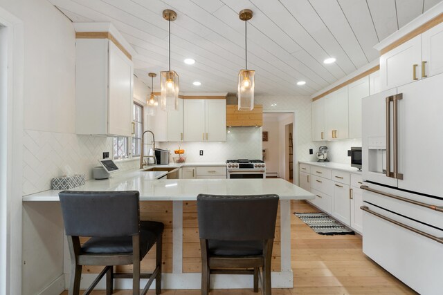 kitchen featuring recessed lighting, a sink, light wood-style floors, high quality appliances, and a peninsula