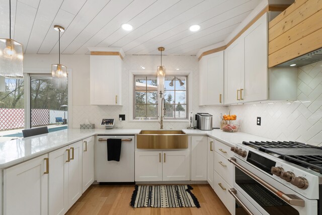 kitchen with light countertops, white cabinets, dishwasher, a sink, and range with two ovens