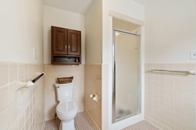 bathroom featuring tile patterned floors, a shower stall, tile walls, a wainscoted wall, and toilet