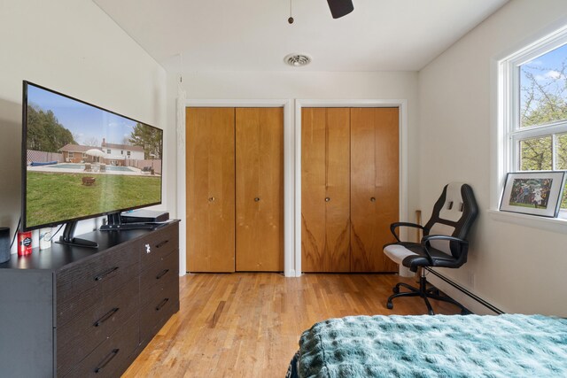 bedroom featuring light wood-type flooring, a ceiling fan, two closets, and a baseboard radiator