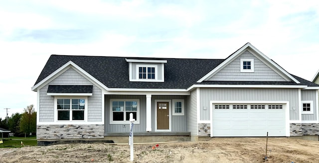 view of front of home featuring stone siding, covered porch, an attached garage, and a shingled roof