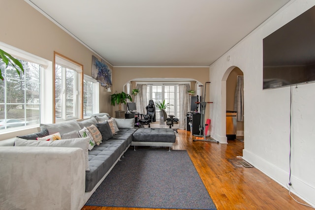 living room with baseboards, crown molding, arched walkways, and wood finished floors