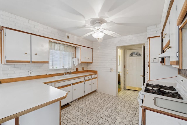 kitchen featuring white gas stove, light floors, light countertops, white cabinetry, and a sink