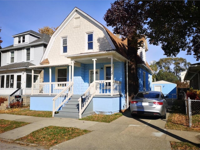 view of front of house featuring driveway, covered porch, fence, and a gambrel roof