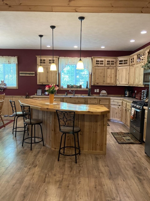 kitchen with a center island, wooden counters, gas stove, a sink, and wood finished floors