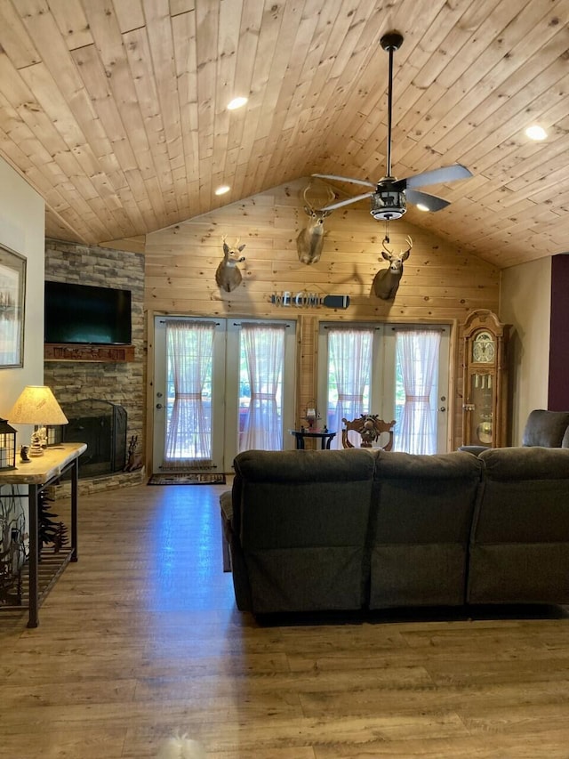 living area featuring lofted ceiling, wooden walls, a stone fireplace, wood finished floors, and wooden ceiling