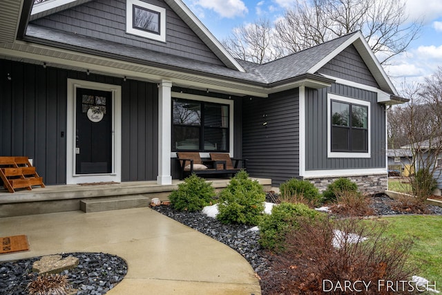 property entrance with covered porch, stone siding, board and batten siding, and roof with shingles