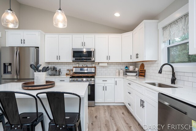 kitchen with decorative light fixtures, light countertops, appliances with stainless steel finishes, vaulted ceiling, and a sink