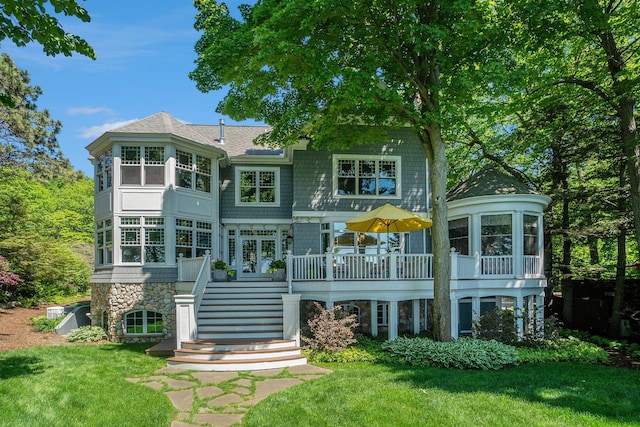 rear view of property with a lawn, stone siding, roof with shingles, stairs, and a deck