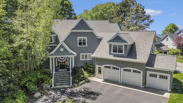 shingle-style home with a garage, roof with shingles, and driveway