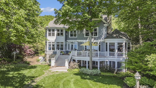 rear view of house with a shingled roof, a chimney, stairs, a deck, and a yard