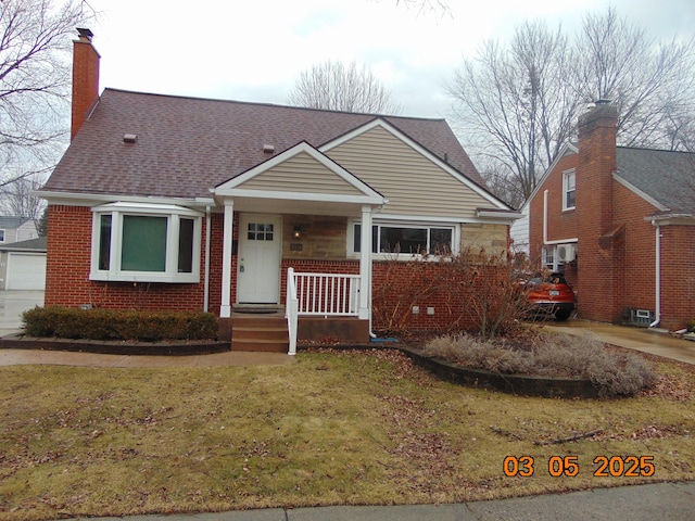 view of front of house featuring brick siding, roof with shingles, a chimney, covered porch, and a front yard