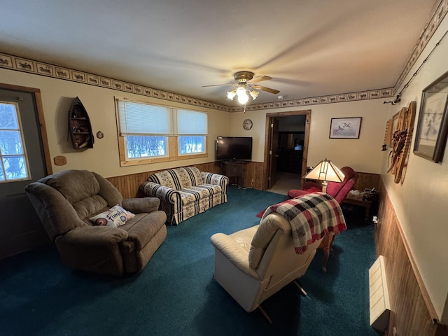 living area featuring carpet floors, a wainscoted wall, wooden walls, and a ceiling fan