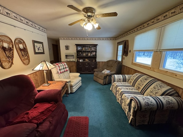 carpeted living area featuring a healthy amount of sunlight, heating unit, ceiling fan, and a wainscoted wall