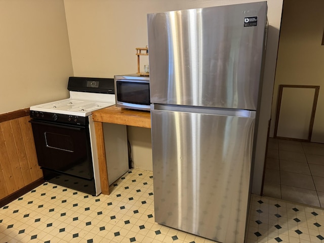 kitchen featuring stainless steel appliances, light countertops, a wainscoted wall, and wood walls