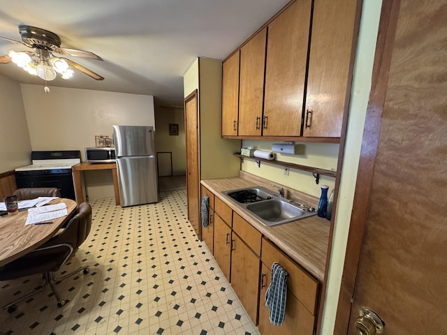 kitchen with brown cabinetry, appliances with stainless steel finishes, light countertops, light floors, and a sink