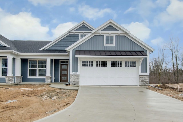 view of front of property with concrete driveway, board and batten siding, a standing seam roof, a garage, and stone siding