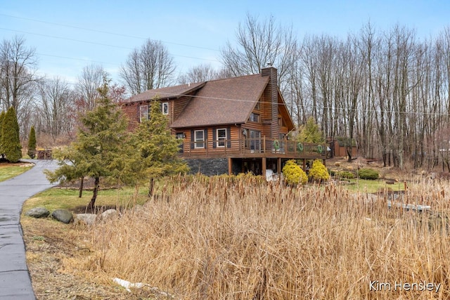 view of side of property with a chimney, roof with shingles, driveway, and a deck