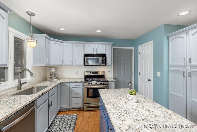 kitchen featuring recessed lighting, wood finished floors, a sink, hanging light fixtures, and appliances with stainless steel finishes