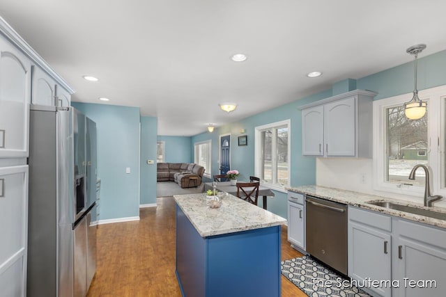 kitchen with a kitchen island, appliances with stainless steel finishes, open floor plan, wood finished floors, and a sink