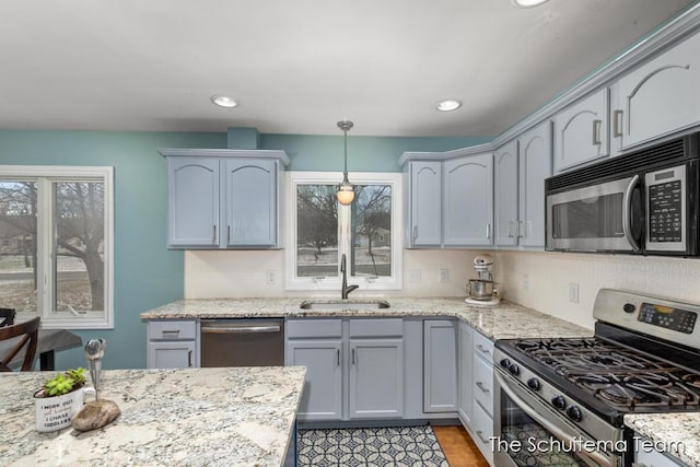 kitchen featuring light stone counters, recessed lighting, a sink, hanging light fixtures, and appliances with stainless steel finishes