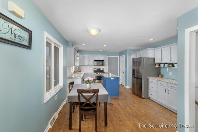 kitchen with baseboards, appliances with stainless steel finishes, a center island, white cabinetry, and a sink