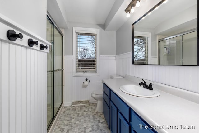 bathroom with toilet, visible vents, vanity, wainscoting, and a shower stall