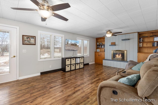 living room with ceiling fan, built in shelves, a large fireplace, wood finished floors, and baseboards