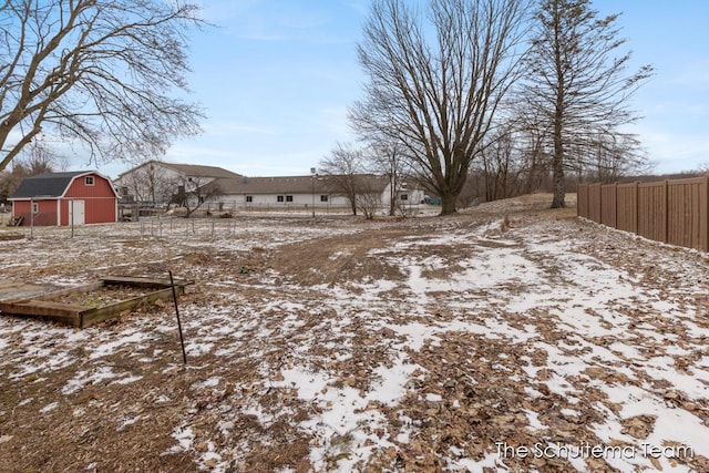 snowy yard featuring an outbuilding, fence, and a barn