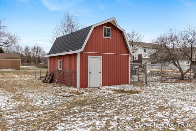 snow covered structure featuring an outbuilding, a barn, and fence