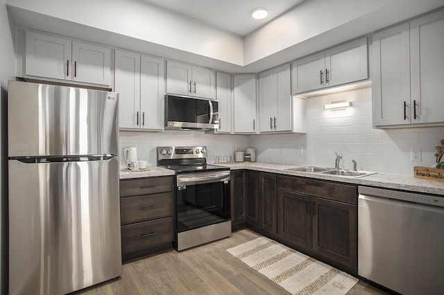 kitchen featuring decorative backsplash, stainless steel appliances, dark brown cabinets, light wood-style floors, and a sink