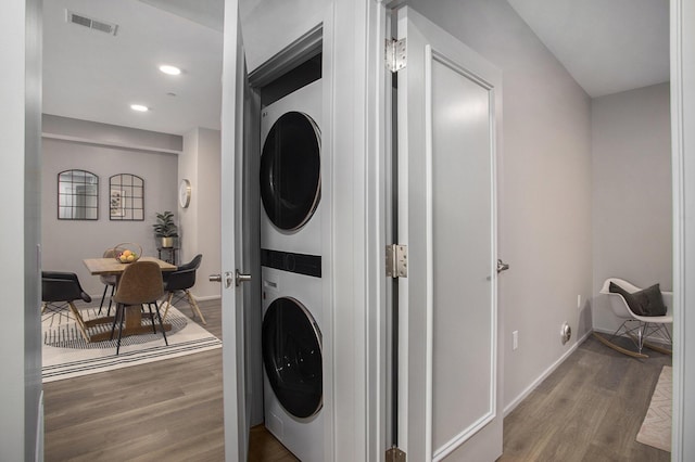 washroom with laundry area, wood finished floors, visible vents, baseboards, and stacked washer / drying machine