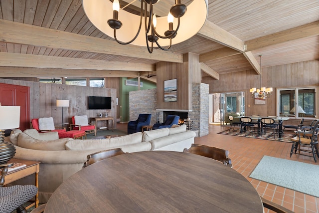 living room with wooden walls, a stone fireplace, beam ceiling, and a notable chandelier