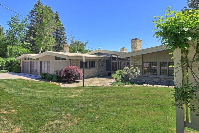 exterior space with concrete driveway, a front lawn, a chimney, and stone siding