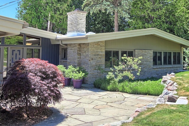 exterior space with stone siding, a patio area, and a chimney